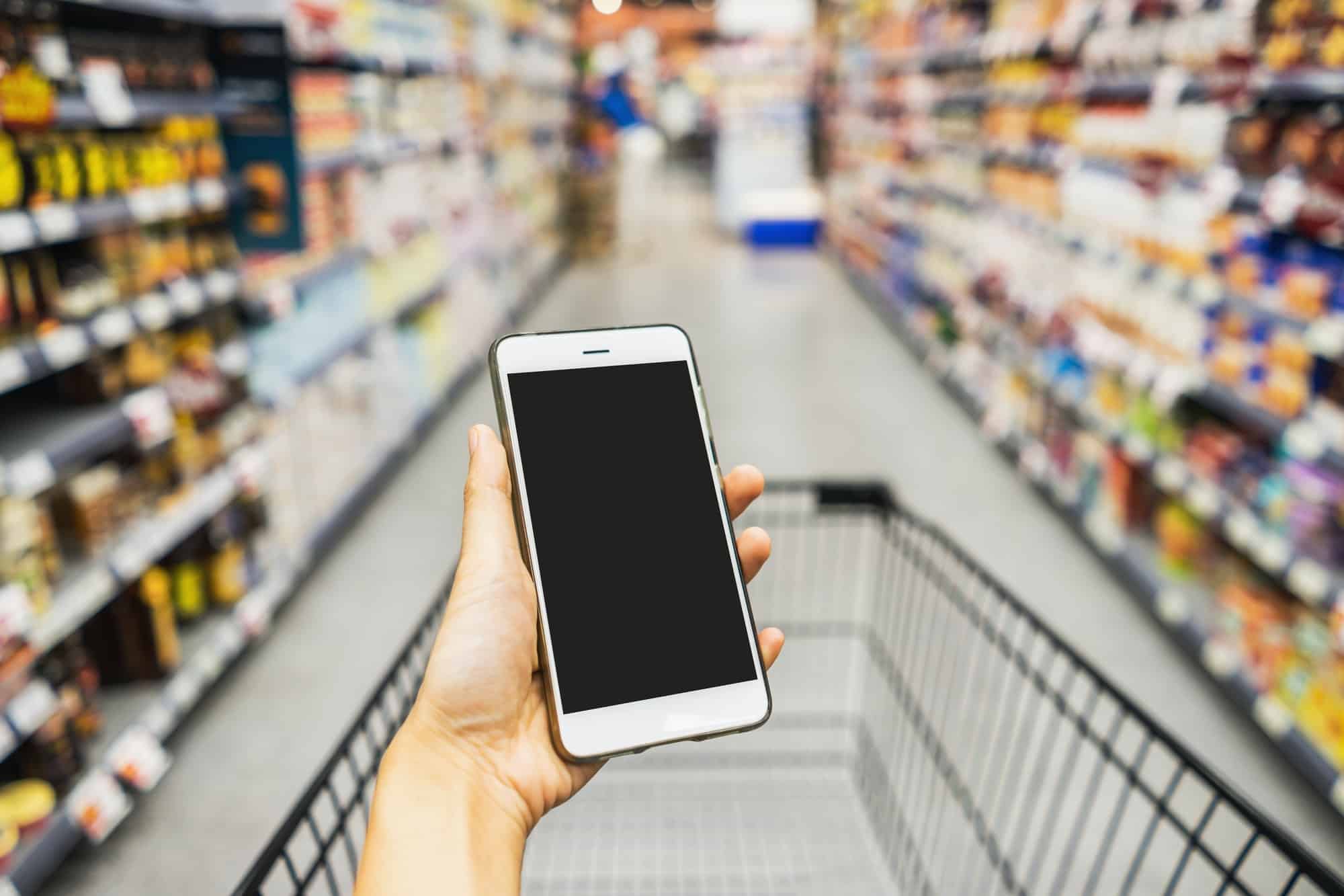 Hand holding smart phone with pushcart in supermarket