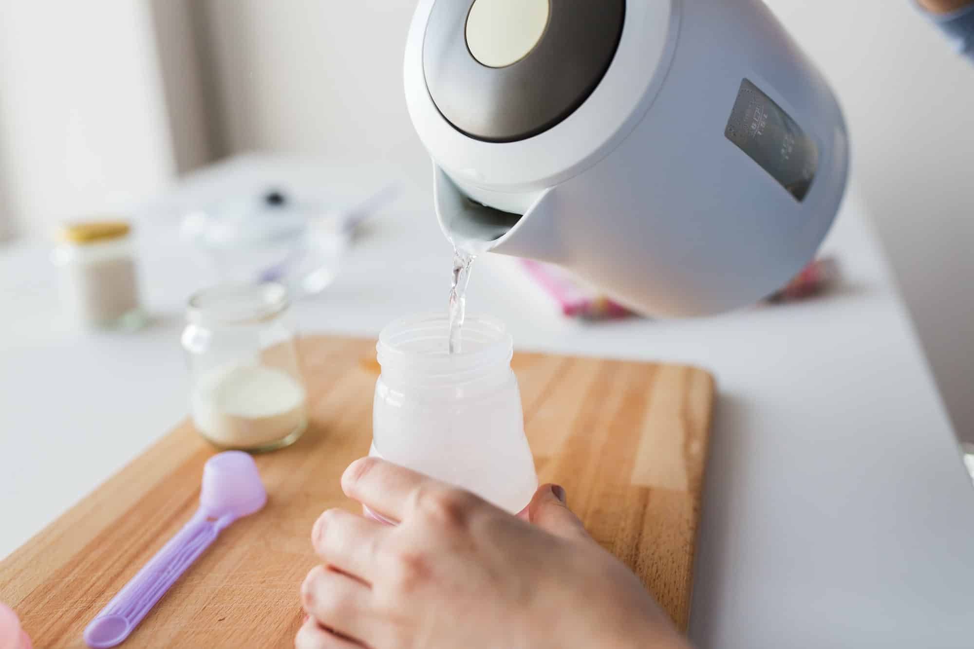 hands with kettle and bottle making baby milk